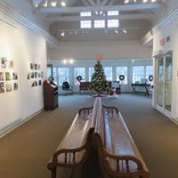 Gallery with 2 benches and pictures on wall.  Facing bow of windows with Christmas tree. 